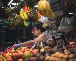 Photo by Daniel Angele on Unsplash The image shows a food stand with a woman selling fruits.